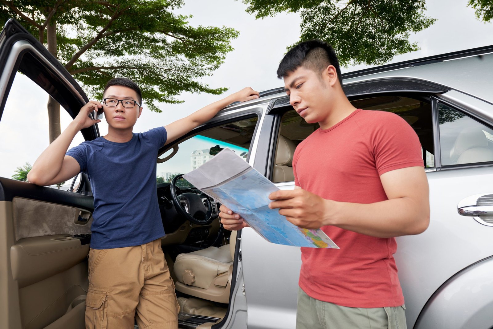Người đàn ông châu Á đứng cạnh ô tô của mình gọi điện thoại bạn bè kiểm tra bản đồ